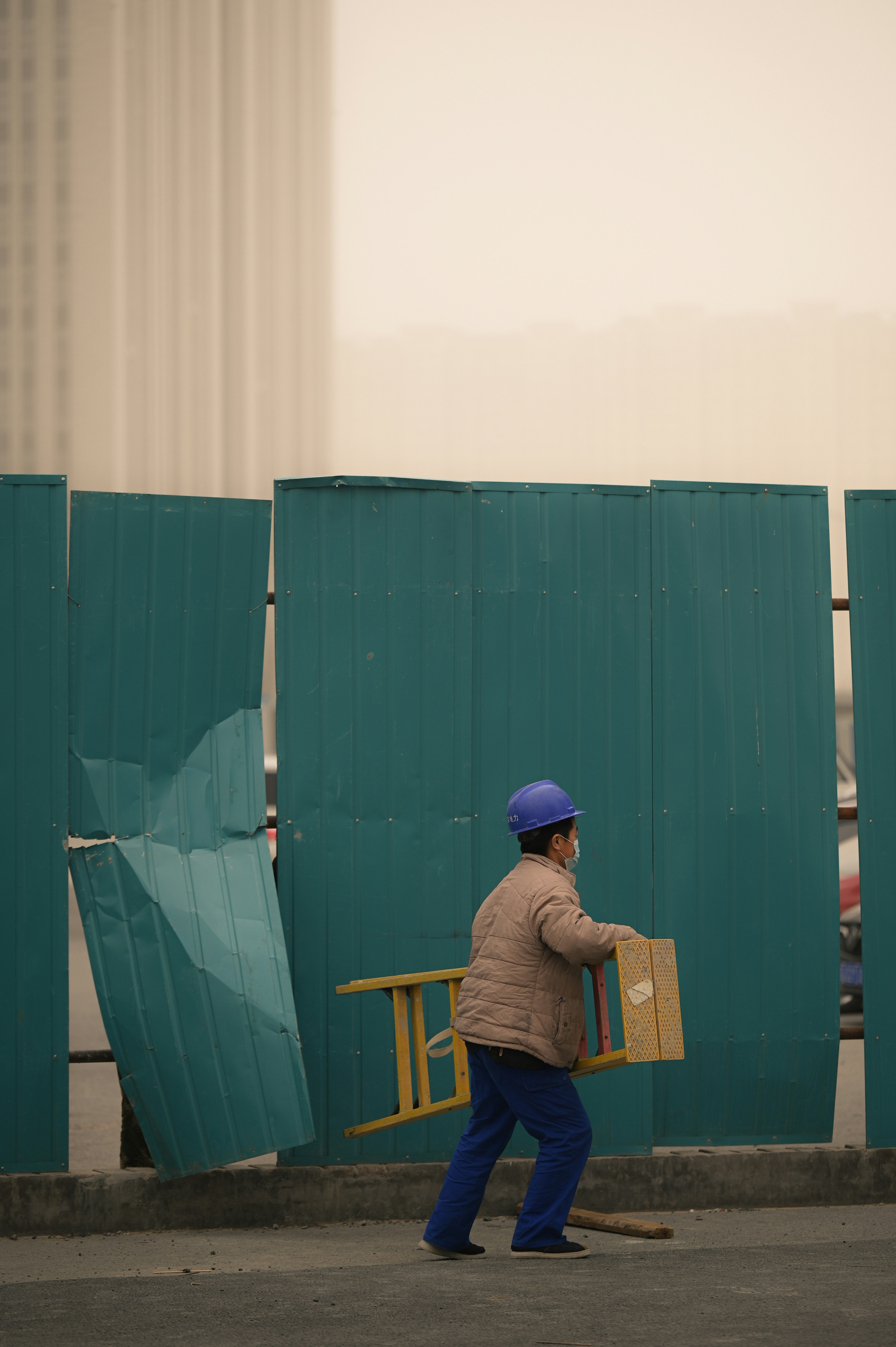 man in brown long sleeve shirt and blue fitted cap standing beside green metal fence